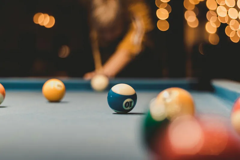 A view across pool balls on blue felt with a player beyond